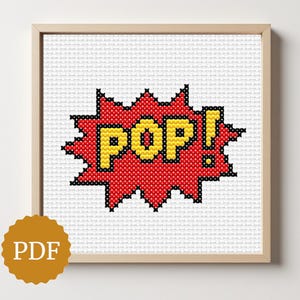 May include: A framed cross-stitch artwork displaying the word "POP!" in yellow within a red burst shape. The design is set against a white background and framed in light wood. The PDF logo is in the bottom left corner.