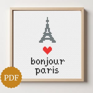 Może przedstawiać: Oprawiona haftem krzyżykowym z Wieżą Eiffla, czerwonym sercem i napisem "bonjour paris". Projekt znajduje się na białym tle, z logo PDF w lewym dolnym rogu. Rama jest drewniana.