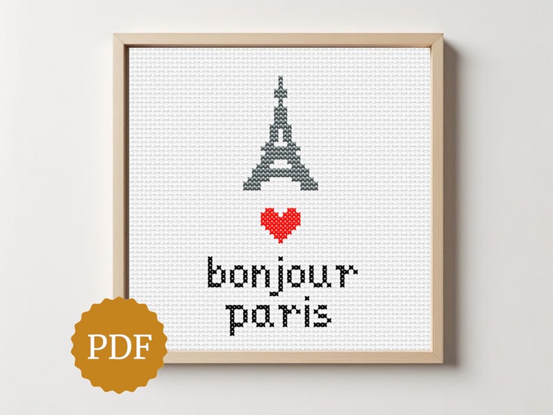 Może przedstawiać: Oprawiona haftem krzyżykowym z Wieżą Eiffla, czerwonym sercem i napisem "bonjour paris". Projekt znajduje się na białym tle, z logo PDF w lewym dolnym rogu. Rama jest drewniana.