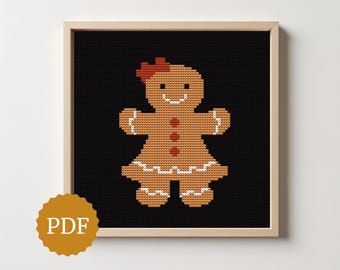 May include: A framed cross-stitch pattern of a gingerbread person on a black background. The gingerbread person is brown with white icing details, red bow, and red buttons. The frame is light brown, and a PDF logo is in the lower left corner.