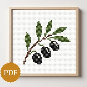 以下が含まれることがあります： オリーブの枝を描いた額入りのクロスステッチパターン。オリーブは黒、葉は緑、枝は茶色です。アートワークは白い背景にあり、薄茶色の木製フレームに入っています。PDFロゴが左下にあります。