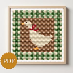 Könnte beinhalten: Kreuzstich-Kunstwerk einer weißen Gans mit roter Schleife, vor braunem Hintergrund und umrahmt von einem grün-weiß karierten Rand. Das Kunstwerk befindet sich in einem Holzrahmen. Ein PDF-Symbol befindet sich in der unteren linken Ecke.
