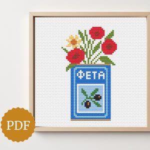 May include: Cross-stitch artwork featuring a blue container labelled "FETA" with red poppies, yellow flowers, and green foliage. The container has an olive branch design. The artwork is in a wooden frame.
