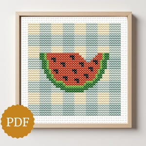 May include: Cross-stitch art of a watermelon slice with a bite taken out, set against a blue and yellow checkered background. The watermelon is red with black seeds and green rind. The artwork is framed in a light wood frame. A PDF icon is in the lower left corner.