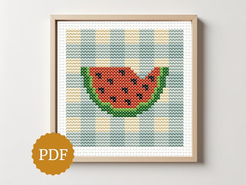 May include: Cross-stitch art of a watermelon slice with a bite taken out, set against a blue and yellow checkered background. The watermelon is red with black seeds and green rind. The artwork is framed in a light wood frame. A PDF icon is in the lower left corner.
