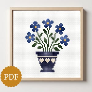 Puede incluir: Patrón de punto de cruz de flores azules en un jarrón azul marino con un borde crema, enmarcado en madera. El icono PDF está en la esquina inferior izquierda. Las flores tienen centros amarillos y tallos verdes.