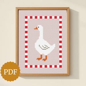 May include: Cross-stitch artwork of a white goose with orange feet and beak, framed by a red and white checkered border. The artwork is set against a light pink background and framed in a wooden frame. The image has a PDF icon.