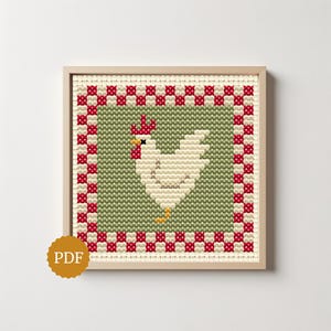 May include: A square cross-stitch pattern featuring a white chicken with a red comb and wattle, centered on a sage green background. The design is framed by a red and white checkered border and is presented within a light wood frame.