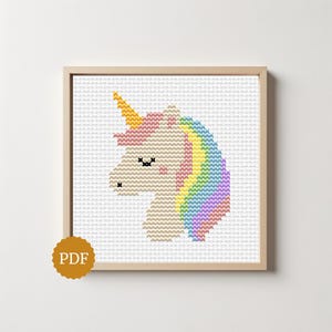 May include: A cross-stitch pattern of a unicorn head in a light wooden frame. The unicorn features a yellow horn, a pink mane, and a rainbow-colored tail and mane section. The design is set against a white grid background with a gold PDF icon.