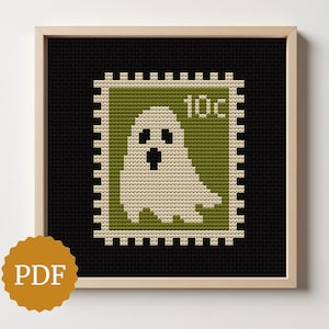 Op de afbeelding: Een ingelijst kruissteekontwerp met een spookzegel van 10¢. De postzegel is groen en crème op een zwarte achtergrond. De lijst is van licht hout. Het PDF-logo staat linksonder. Geschikt voor Halloween.