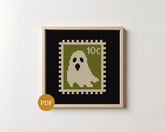 Puede incluir: Un patrón de punto de cruz enmarcado con un diseño de sello postal que muestra un fantasma blanco sobre un fondo verde. El sello incluye el texto 10c en la esquina superior derecha. El diseño está sobre un fondo negro en un marco de madera clara.