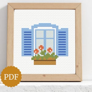 Può includere: Schema a punto croce di una finestra blu con persiane, una fioriera e fiori arancioni. L'opera è incorniciata in una cornice di legno chiaro. Un'icona PDF si trova nell'angolo in basso a sinistra.