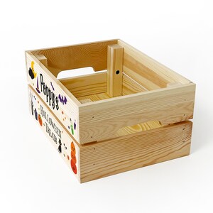 May include: A rectangular light-coloured wooden crate with cut-out handles on the sides. The front panel features the text "Poppy's HALLOWEEN TREATS" in black lettering, surrounded by colourful illustrations of pumpkins, a black cat, a bat, and a witch hat.