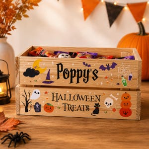 May include: A rectangular wooden crate filled with assorted sweets, featuring the printed text "Poppy's HALLOWEEN TREATS" alongside colourful illustrations of a crescent moon, witch hat, bats, spider web, ghost, tombstone, pumpkins, and a black cat.