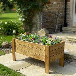 May include: A wooden rectangular planter box filled with a variety of colourful flowers. The planter is made of light brown wood and stands on four legs. The flowers include purple, yellow, and white blooms.