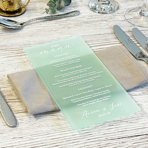 May include: A light blue menu card with white text. The menu includes a starter, main course, dessert, and the names "Aaron & Jess" and the date "29.07.23".