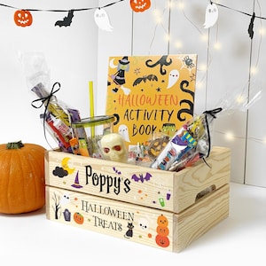 May include: A light-coloured wooden crate with the text Poppy's Halloween Treats, containing a Halloween activity book, a clear tumbler with a yellow straw, a plastic skull, and assorted sweets in clear bags tied with black ribbon.