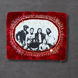 May include: A red velvet patch with a gold embroidered oval frame. Inside the frame is a black and white image of a group of people. The frame is surrounded by gold embroidered rays and stars.