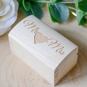 May include: A wooden ring box with the words "Mr. & Mrs." engraved on the top, with a heart shape in the middle.