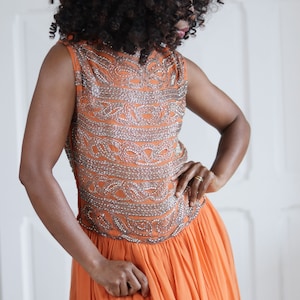 Peut inclure: Robe orange sans manches avec un corsage perlé. Le corsage présente une broderie argentée complexe. La jupe est une conception fluide et plissée. La robe est une pièce vibrante, idéale pour les occasions spéciales.