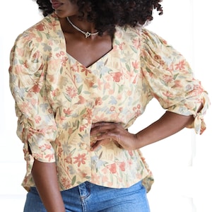 May include: A yellow floral print blouse with puffed sleeves and a button-up front. The blouse has a V-neckline and a fitted waist.