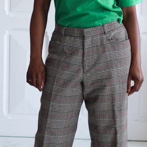 May include: A person wearing a green t-shirt with "WIMBLEDON THE CHAMPIONSHIPS POLO TENNIS" text and brown plaid pants. The pants have a classic plaid pattern with red and black accents.