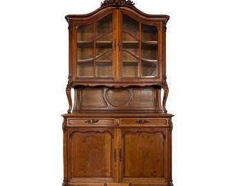 Könnte beinhalten: Ein antiker zweigeteilter Holzschrank mit Glastüren und geschnitzten Details. Der obere Teil hat Glastüren und Regale, während der untere Teil zwei massive Holztüren mit geschnitzten Details hat. Der Schrank ist aus dunklem Holz gefertigt und hat eine reiche, antike Oberfläche.