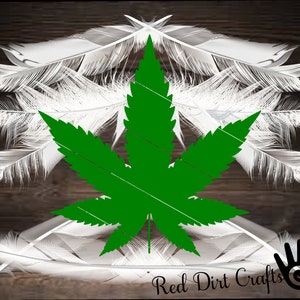 May include: A green marijuana leaf with white feathers surrounding it. The background is a dark wood grain. The text "Red Dirt Crafts" is at the bottom of the image.