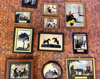 May include: A collection of framed silhouette art pieces, each depicting scenes of people, animals, and landscapes. The frames vary in shape and size, with colors including black, gold, and brown. The art is mounted on a textured, reddish-orange background.