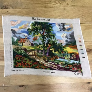 Puede incluir: Un tapiz cosido a mano con las palabras "MA CAMPAGNE" en la parte superior. El tapiz representa un paisaje rural con una casa, árboles y un río. También se ven las palabras "made in france".