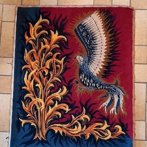 May include: A rectangular tapestry featuring a stylized bird with outstretched wings. The bird is primarily blue and white against a red background. A golden-yellow plant design is on the left side, with a dark blue border.