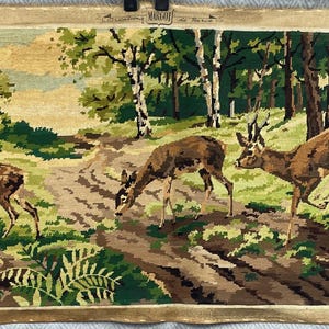 May include: A rectangular needlepoint tapestry featuring a forest scene with three deer in a clearing. The landscape includes green ferns, brown dirt paths, and white-barked birch trees. The top center displays the text Margau de Paris.
