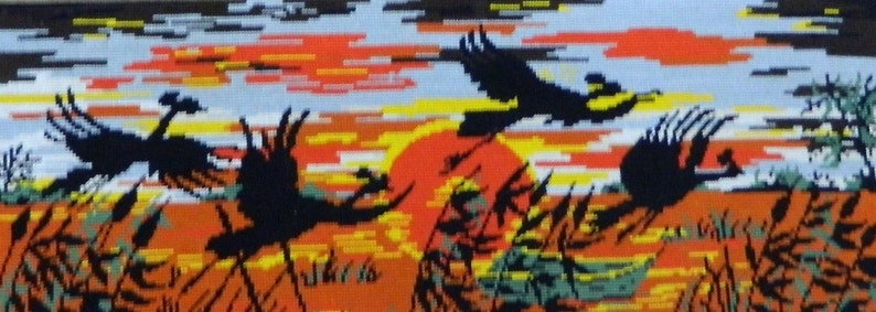May include: A needlepoint tapestry depicting a sunset scene with four silhouetted birds in flight. The artwork features a vibrant color palette of orange, yellow, and black, with a small boat visible in the distance. The tapestry is a landscape scene.