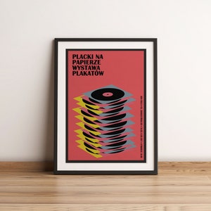 May include: A black framed poster with a red background and the text "Placki na Papierze Wystawa Plakatow". The poster features a stack of black vinyl records with yellow and grey accents.