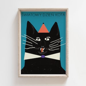 May include: A black cat wearing a red party hat and a white bow tie with a purple accent. The cat has a tongue sticking out and is looking directly at the viewer. The background is a teal blue color. The text "ŚWIATOWY DZIEŃ KOTA" is written in black at the top of the image.
