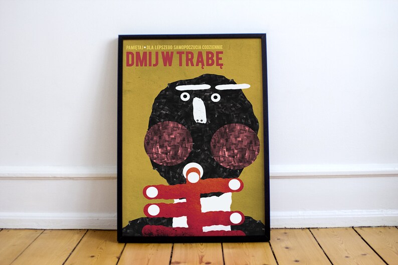 May include: A yellow and black poster with a cartoon face and the text "DMJW TRABĘ". The poster is framed in black.