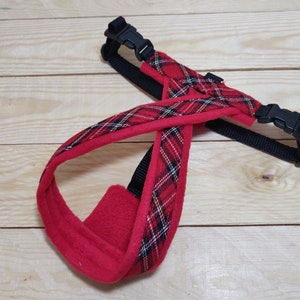 May include: Red and black plaid dog harness with a fleece lining. The harness has two adjustable straps with black buckles.