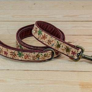 May include: A brown and beige dog lead with a cork-like fabric and a gold-toned metal clasp. The lead has a pattern of leaves and flowers.