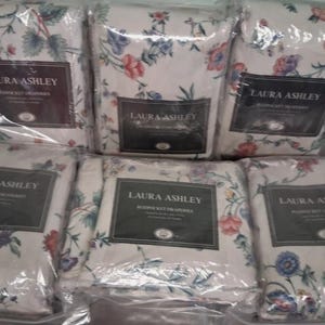 Op de afbeelding: Verschillende verpakte Laura Ashley beddengoedsets. De sets tonen een bloemenpatroon met rode, blauwe en gele bloemen op een witte achtergrond. Elke verpakking heeft een label met het Laura Ashley logo. De tekst "VIEWED TODAY" is zichtbaar.