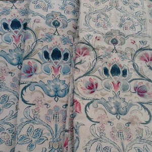 May include: A close-up of a fabric with a floral pattern. The fabric is beige with blue, pink, and green flowers. The fabric is folded in half and the edges are visible.