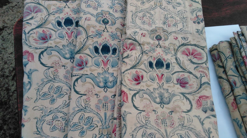 May include: A close-up of a fabric with a floral pattern. The fabric is beige with blue, pink, and green flowers. The fabric is folded in half and the edges are visible.
