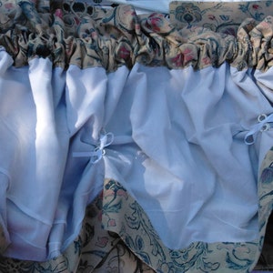 May include: A white sheer curtain with a floral patterned border. The curtain has a gathered look and is tied back with white ribbon.