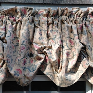 Puede incluir: Una cenefa de color crema con un patrón floral en tonos rosa, azul y verde. La cenefa tiene un volante fruncido en la parte superior y está hecha de una tela suave y texturizada.