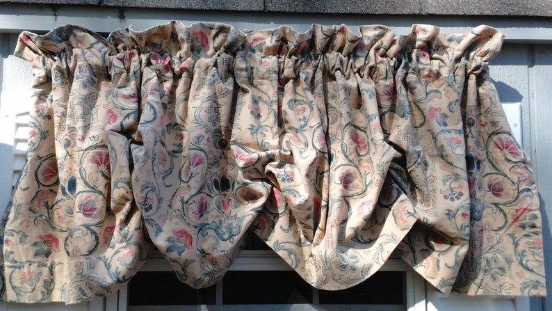 May include: A cream-colored valance with a floral pattern in shades of pink, blue, and green. The valance has a gathered ruffle at the top and is made of a soft, textured fabric.