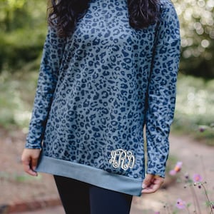 May include: A blue and black leopard print long-sleeved top with a monogrammed detail on the bottom hem.