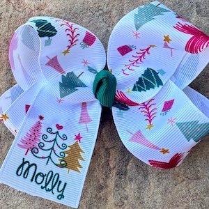 May include: White Christmas tree hair bow with a green center and a personalized name tag that says "Molly".