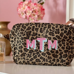 May include: A brown and black leopard print makeup bag with the letters MTM embroidered in pink and light blue.