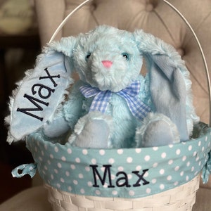 May include: A blue plush bunny with a blue and white gingham bow sits in a white wicker basket with a blue and white polka dot lining. The basket and bunny are personalized with the name "Max".