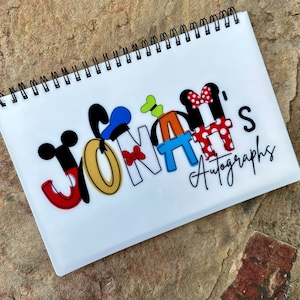 May include: A white spiral bound autograph book with the name "JONAH'S Autographs" written in black script with colorful cartoon characters forming the letters of the name.
