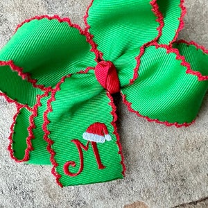 May include: Green Christmas bow with red trim and a white and red Santa hat with the letter "M" embroidered on it.